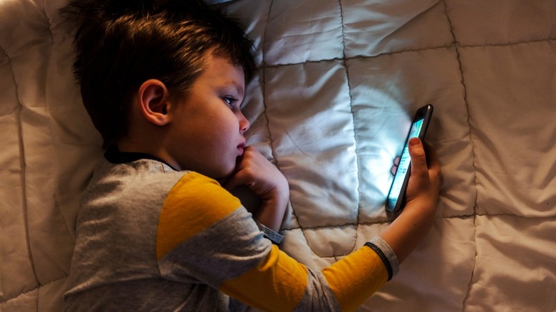 A kid using a phone while laying in bed