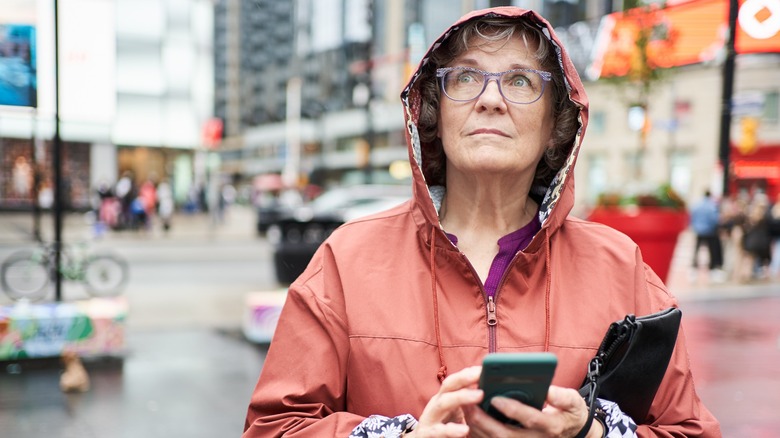 Mature woman outside in a rain coat with phone in hand