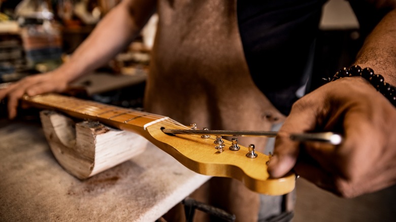 A luthier working on an electric guitar headstock.